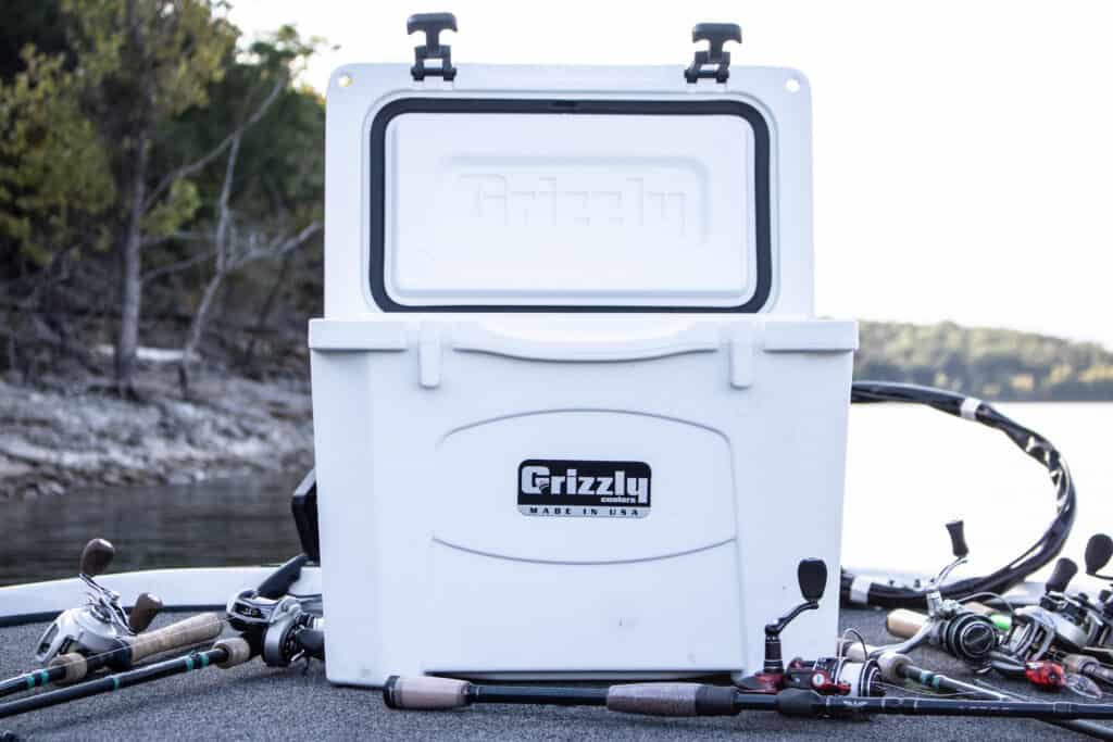 white grizzly 15 boat cooler sitting on bow of boat open with fishing rods and reels on either side and water and water front scenery in background
